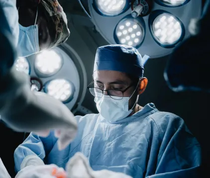 Surgeon in scrubs and mask operating under overhead surgical lights