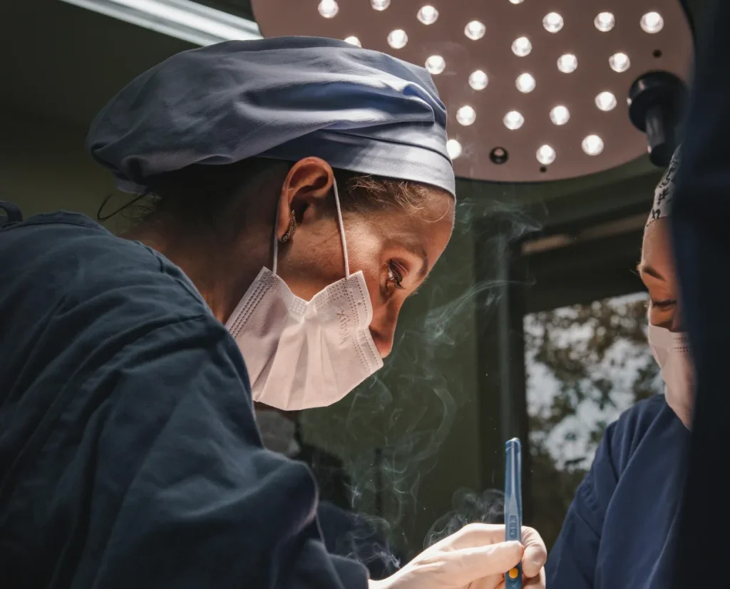Anesthesia provider in a surgical cap and mask leaning over a patient during a procedure