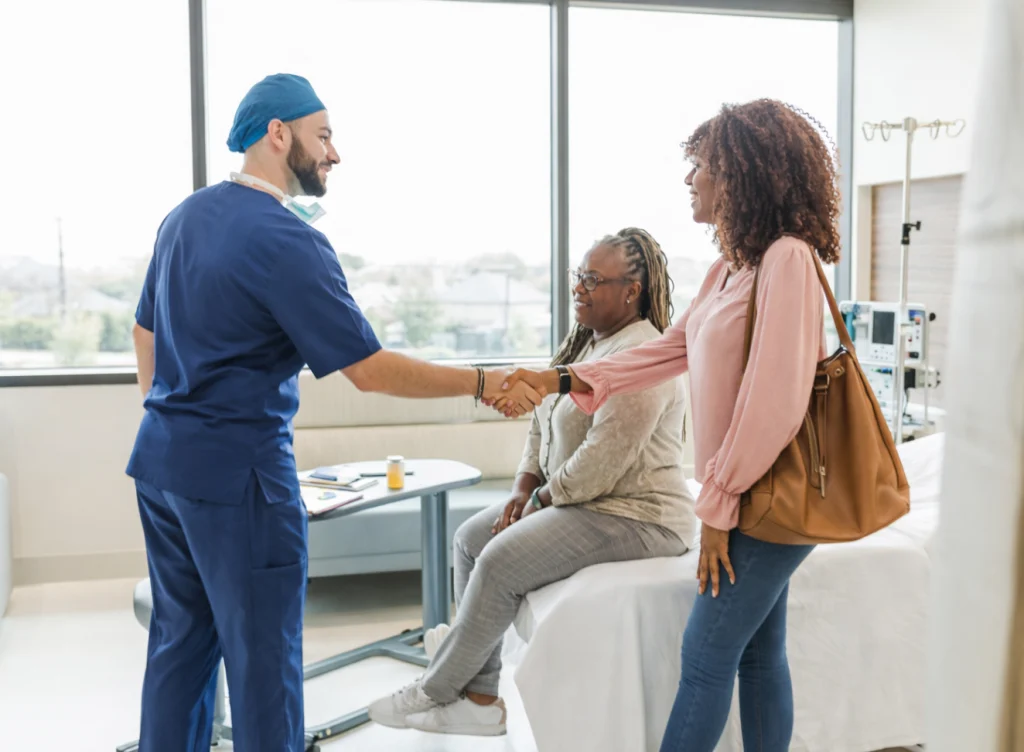 Clinician in scrubs shaking hands with a patient and her companion in an exam room